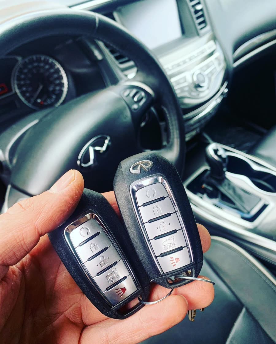 Two Infiniti smart keys held up inside the car, with the steering wheel and dashboard behind