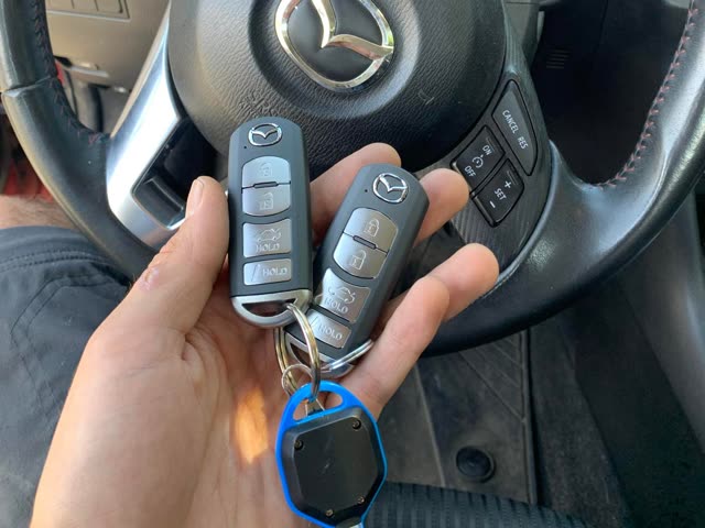 Two Mazda flip keys held in front of a Mazda steering wheel