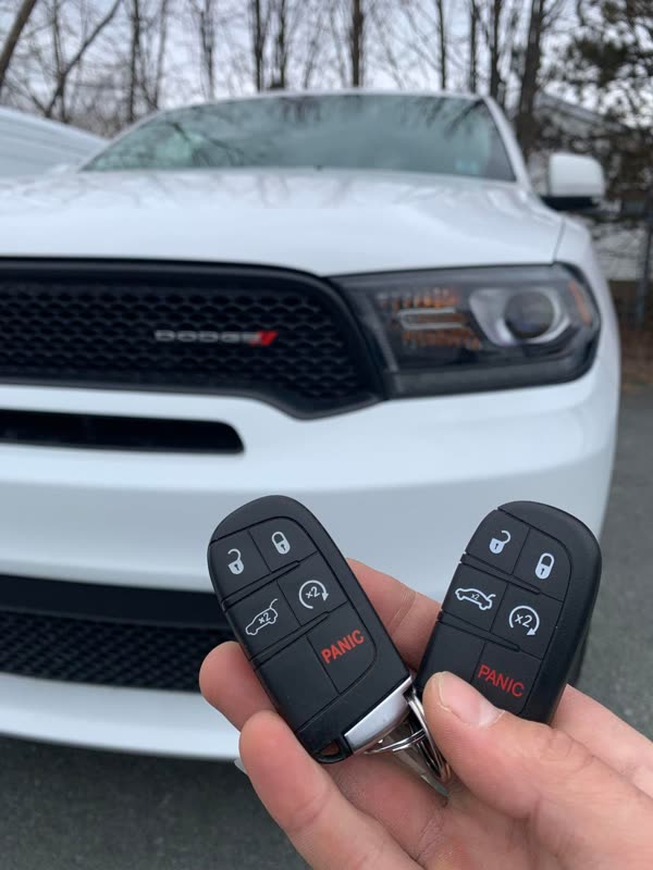 Two Dodge key fobs with remote start held in front of a white Dodge Durango