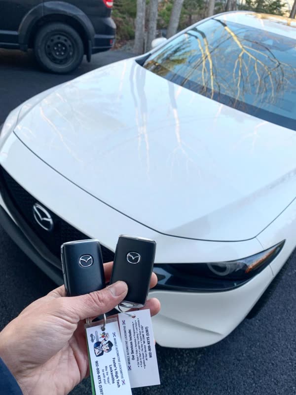 Hand holding two new Mazda smart keys in front of a white Mazda