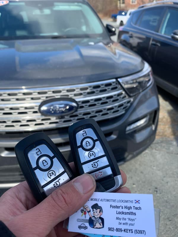 Two Ford push-to-start fobs held up in front of a grey Ford Explorer