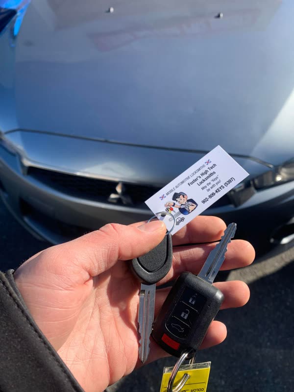 Mitsubishi remote head key and a spare key blade held in front of a grey Mitsubishi